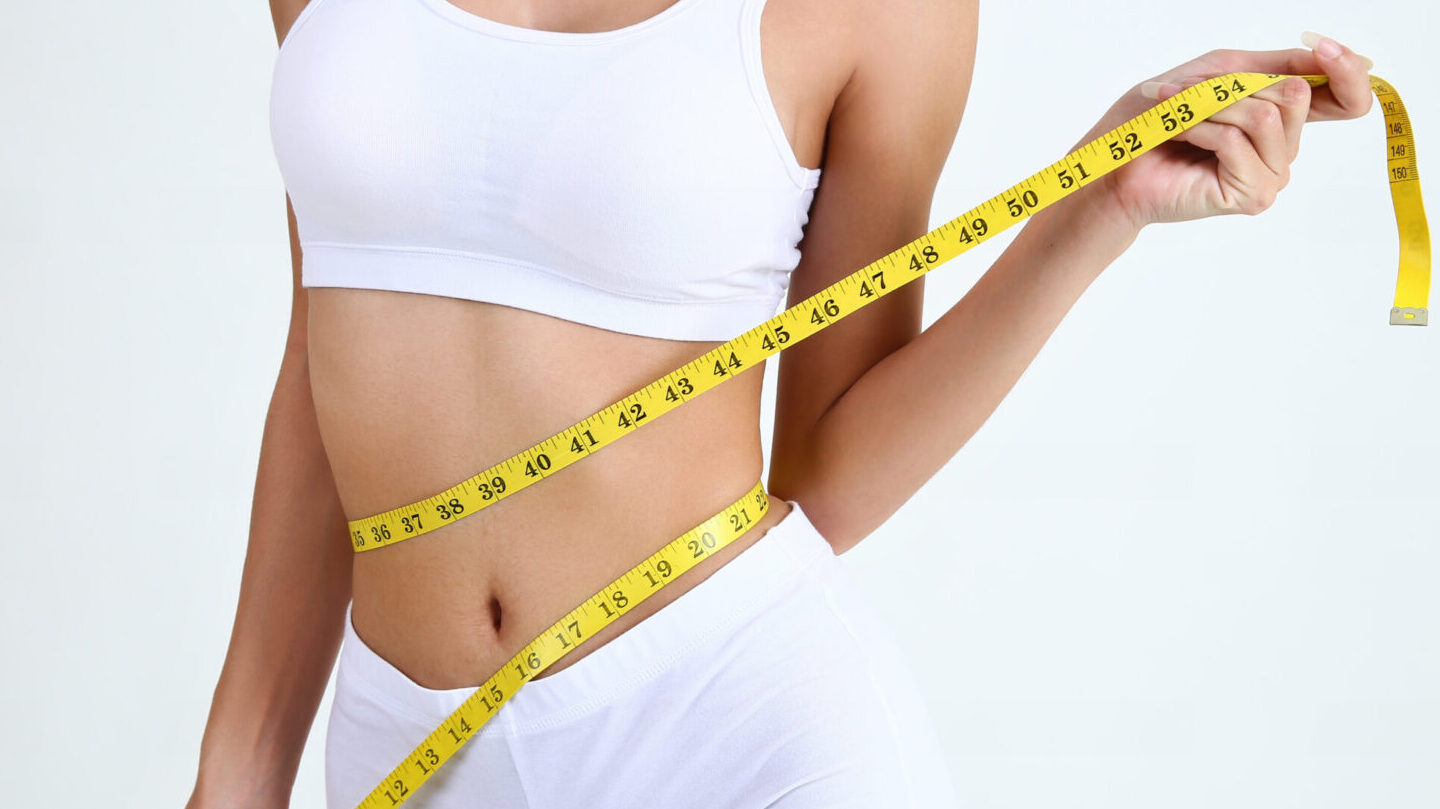 Close up slimming female with beautiful body and measuring her waistline  with measure tape on white background and copy space